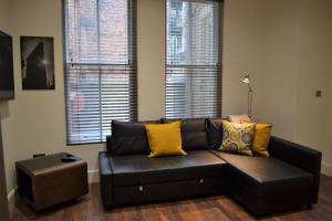 a black leather couch in a living room with two windows at OnPoint - 2 Bed Apartment City Centre Ideal Location! in Nottingham