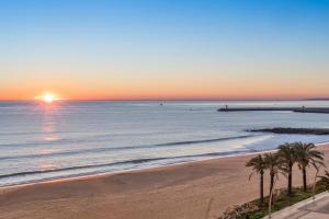 a sunset over the ocean with palm trees on a beach at Dom Jose Beach Hotel (Plus) in Quarteira