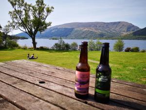 two bottles of beer sitting on a picnic table near a lake at Rowardennan Youth Hostel in Rowardennan