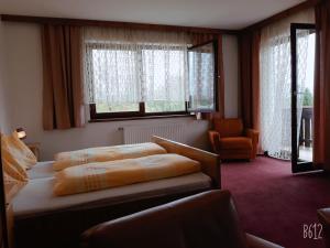 a bedroom with a bed and a chair and windows at Ferienpension Garni Hubert Rigelnik in Sankt Kanzian