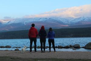 three people standing on the beach with a dog at Cairngorm Lodge Youth Hostel in Loch Morlich