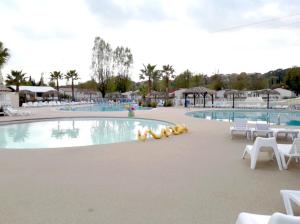a large swimming pool with white chairs and tables at GRAND MOBILEHOME PROCHE COMMODITE FO10 in Fréjus
