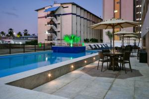 a pool with a table and chairs and an umbrella at Littoral Gold Flat in João Pessoa