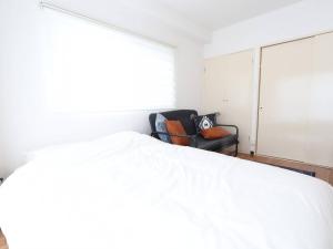 茅ヶ崎市にある湘南茅ヶ崎/湘南ライフの楽しめるアパートメントのベッドルーム(白いベッド1台、黒い椅子付)