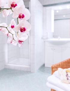 a white bathroom with a white sink and pink orchid at Landhaus Pannonia in Mörbisch am See