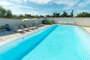 a large swimming pool with chairs and an umbrella at Hôtel et Résidence de la Transhumance in Saint-Martin-de-Crau