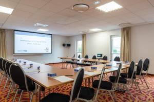 a conference room with tables and chairs and a projection screen at The Originals City, Hôtel Acadine, Pont-Audemer in Pont-Audemer