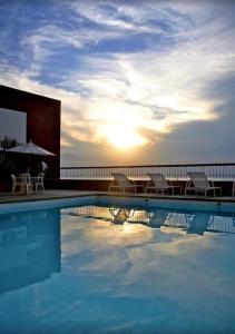 uma piscina com cadeiras e um guarda-sol e o pôr-do-sol em Flat Privativo Sol Victoria Marina em Salvador