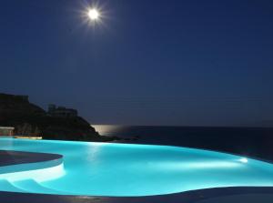 una piscina notturna con la luna sull'oceano di Mykonos Pantheon a Kalo Livadi