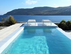 a swimming pool with two chairs and the water at Mykonos Pantheon in Kalo Livadi