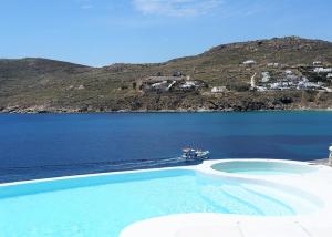 a swimming pool next to a body of water with a boat at Mykonos Pantheon in Kalo Livadi