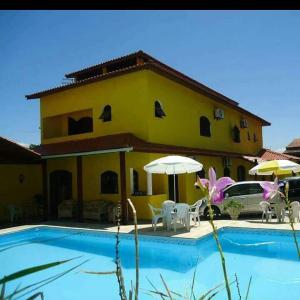 una casa gialla con piscina, sedie e ombrelloni di Pousada Peruíbe Praia a Peruíbe