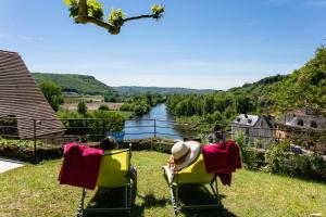 two people sitting in lawn chairs looking out at a river at Au coeur de Beynac, superbe maison du 16ème siècle avec jardin panoramique in Beynac-et-Cazenac