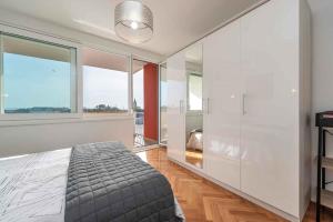 a bedroom with a bed and large windows at Sea the Sunset Apartment in Zadar