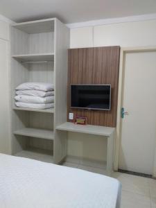 Habitación con cama, TV y estanterías. en Apartamento Lacqua Di Roma, en Caldas Novas