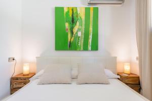 a bedroom with a white bed with a painting above it at Nyumba ya Sun in Cala Tarida