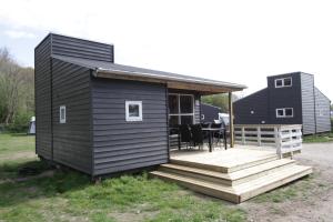 une petite maison noire avec une terrasse couverte et une terrasse dans l'établissement Husodde Strand Camping & Cottages, à Horsens