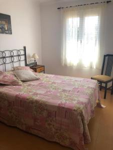 ein Schlafzimmer mit einem Bett mit einer rosa Decke und einem Stuhl in der Unterkunft Apartamento 2ª planta Ca'n Miquel in Cala Galdana