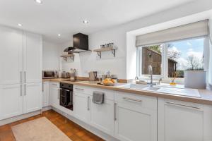 a kitchen with white cabinets and a sink and a window at Harewood Cottage Peak District in Leek