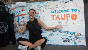 une femme est assise devant un signe de bienvenue au tampa dans l'établissement Finlay Jack's Backpackers, à Taupo