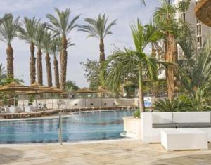 a beach with a large pool and palm trees at Royal Dead Sea - Hotel & Spa in Ein Bokek