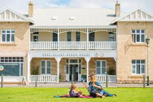 a woman and a child sitting on the grass in front of a building at Port Elliot Beach House YHA in Port Elliot