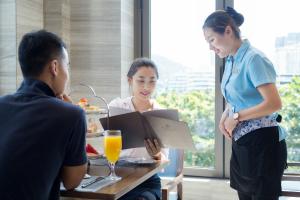 三亞的住宿－三亞大東海酒店，女人和坐在桌子上的男人说话,女人站在桌子前