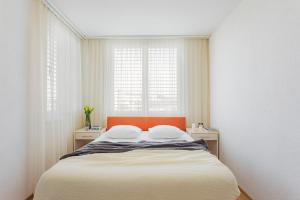 a bedroom with a bed with an orange headboard and two windows at Swiss Star Oerlikon Lodge - Self Check-In in Zürich