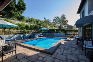 a swimming pool with chairs and an umbrella at The Hamptons Guest House in Durban