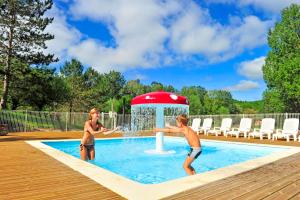 twee jongens spelen in een zwembad met een fontein bij Résidence Goélia Les Cottages du Lac in Coly