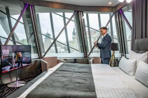 a man in a suit standing next to a bed in a room at Dancing House - Tančící dům hotel in Prague