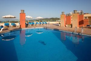 une grande piscine avec des chaises et des parasols bleus dans l'établissement htop Royal Sun Suites #htopFun, à Santa Susanna