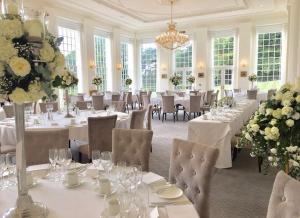 uma grande sala de jantar com mesas e cadeiras brancas em Rushton Hall Hotel and Spa em Kettering