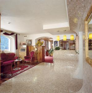 a living room with a tile floor and a living room with chairs at Hotel Olympia in Molveno