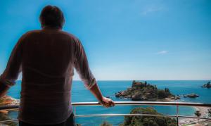 a man standing on a balcony looking at the ocean at Taormina Panoramic Hotel in Taormina