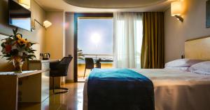 a hotel room with a bed and a desk and a window at Taormina Panoramic Hotel in Taormina