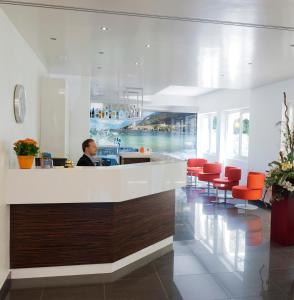 a man sitting at a counter in a lobby with red chairs at Hotel Augusta in Malcesine +86 photos
