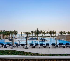 a large swimming pool with chairs and palm trees at Private Beach, Resort Living Kingdom of Sheba in Dubai