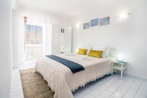 een witte slaapkamer met een groot bed met gele kussens bij Esquina do Mar in Armação de Pêra