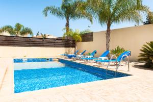een zwembad met blauwe stoelen en palmbomen bij Andina villa close to the sea in Protaras