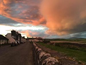 a road with a stone wall and a cloudy sky at Cornmill House, With Outstanding Sea Views In Garlieston in Garlieston