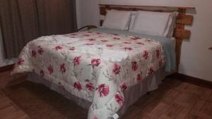 a bed with a white blanket with red flowers on it at Pousada Pinhalense in Santo Antônio do Pinhal