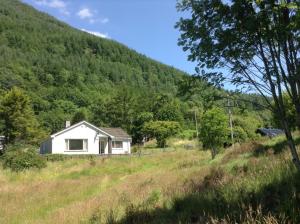 uma casa branca num campo com uma montanha em "An Comaraich - The Sanctuary" em Inverinate