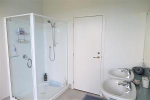 ein weißes Bad mit einer Dusche und einem Waschbecken in der Unterkunft Kakariki Rooms, Kotare House in Tawharanui
