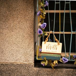 un cartel con flores púrpuras colgando de una pared en HouseNandoor, en Tainan