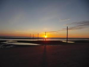 a sunset on a beach with poles in the sand at Haus Kahlke in Sankt Peter-Ording