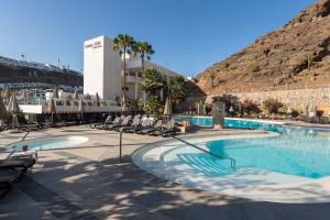 a large swimming pool with chairs and a mountain at Holiday Club Puerto Calma in Puerto Rico de Gran Canaria