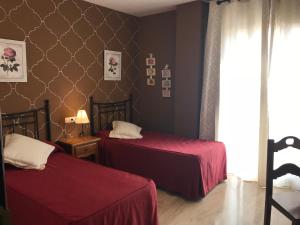 a bedroom with two beds with red sheets and a window at Hotel Las Rosas in Priego de Córdoba