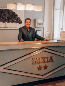 un homme debout derrière un bureau avec un signe lucida dans l'établissement Hotel Luxia, à Paris