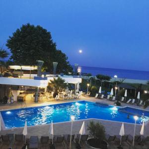 a large swimming pool with chairs and the ocean at night at Anais Hotel in Korinos